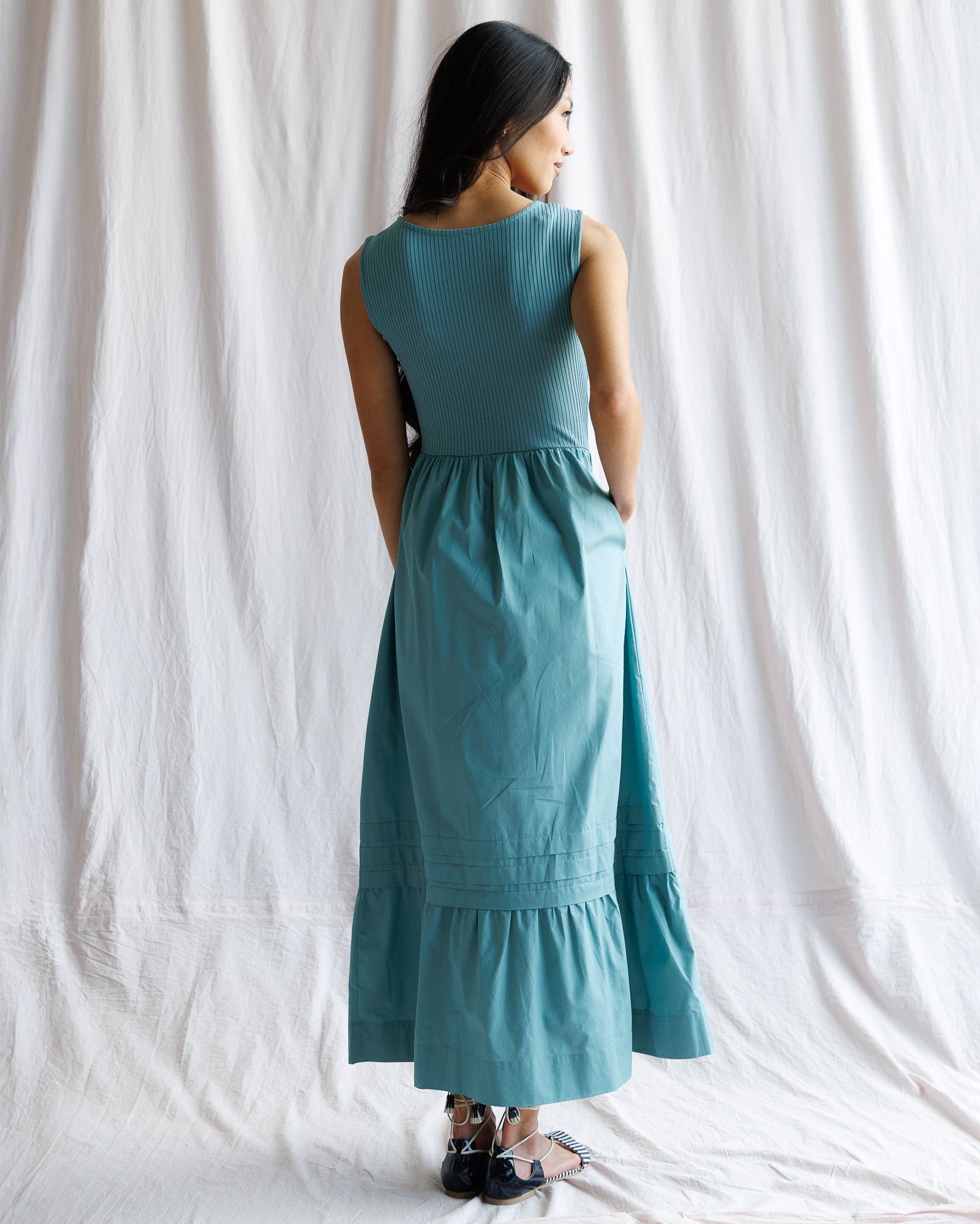Woman wearing a teal dress standing against a white curtain