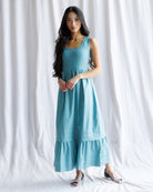 Woman wearing a teal dress against a white curtain background