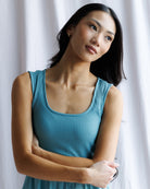 Woman wearing a blue sleeveless top against a white curtain background