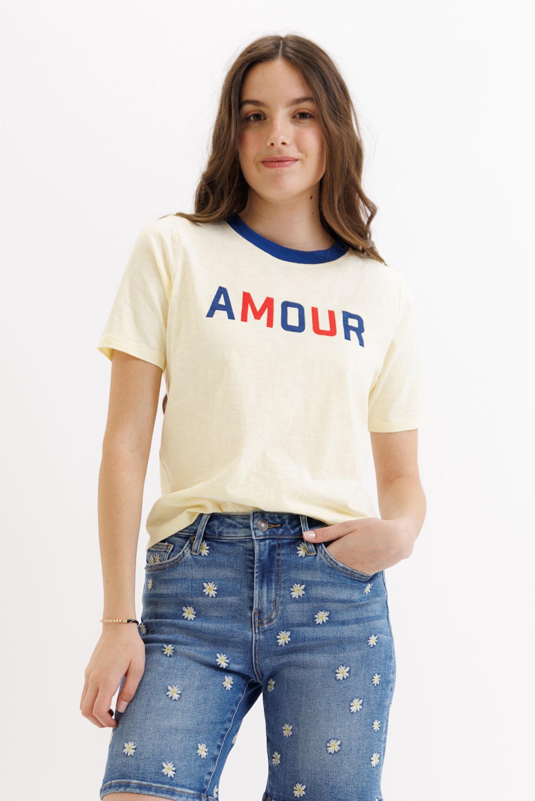 Woman wearing a yellow t-shirt with 'AMOUR' text and blue jeans on a white background