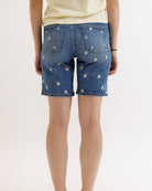 Person wearing blue denim shorts with floral patterns on a white background