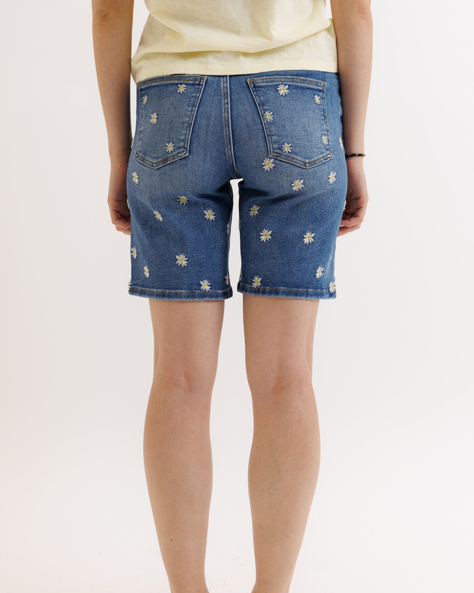 Person wearing blue denim shorts with floral patterns on a white background