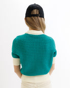 Person wearing a teal knitted cardigan and black cap on a white background