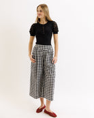 Woman wearing a black top with lace sleeves and checkered pants on a white background