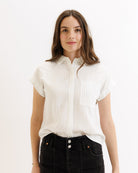 Woman wearing a white striped blouse and black pants on a light background
