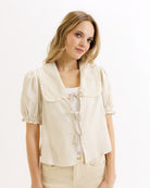 Woman wearing a light beige blouse with puff sleeves on a white background