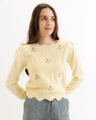 Woman wearing a yellow embroidered sweater against a white background