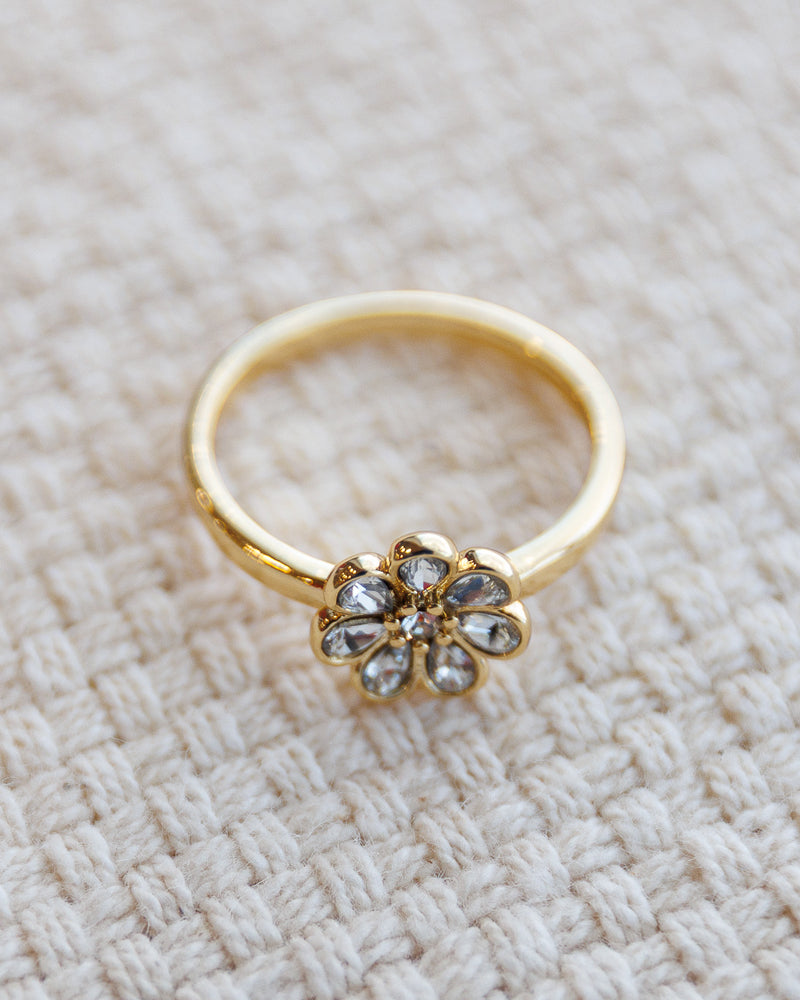 Gold ring with a floral design on a textured beige surface
