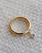 Gold ring with a small gemstone charm on a textured beige surface
