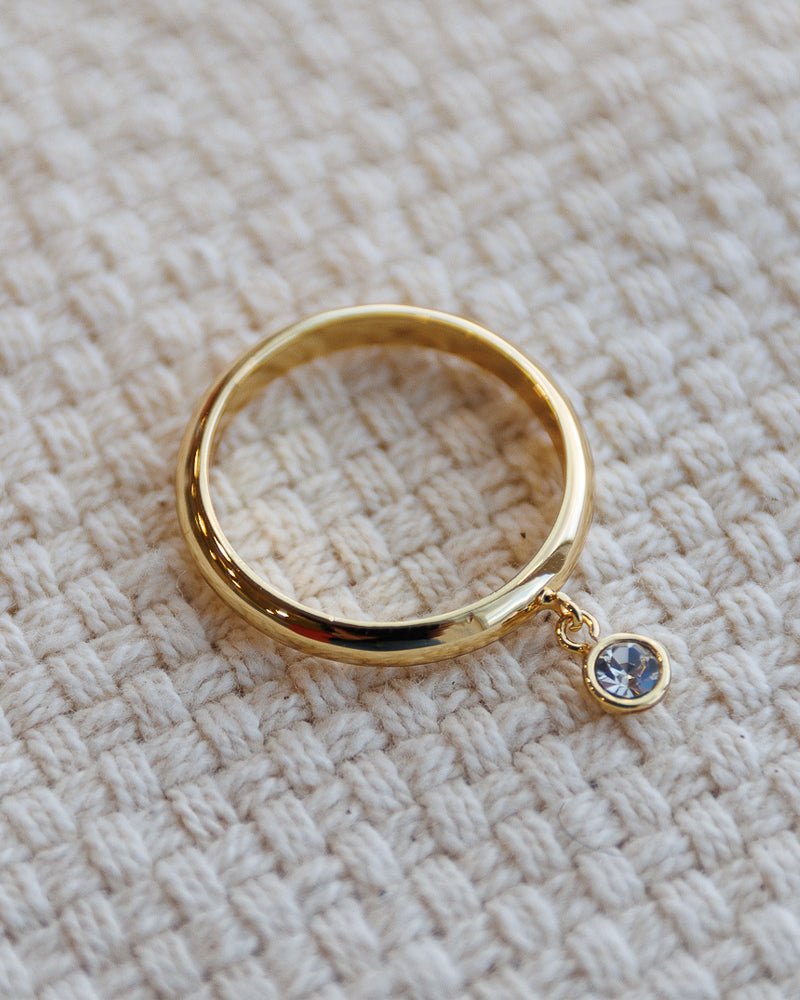Gold ring with a small gemstone charm on a textured beige surface