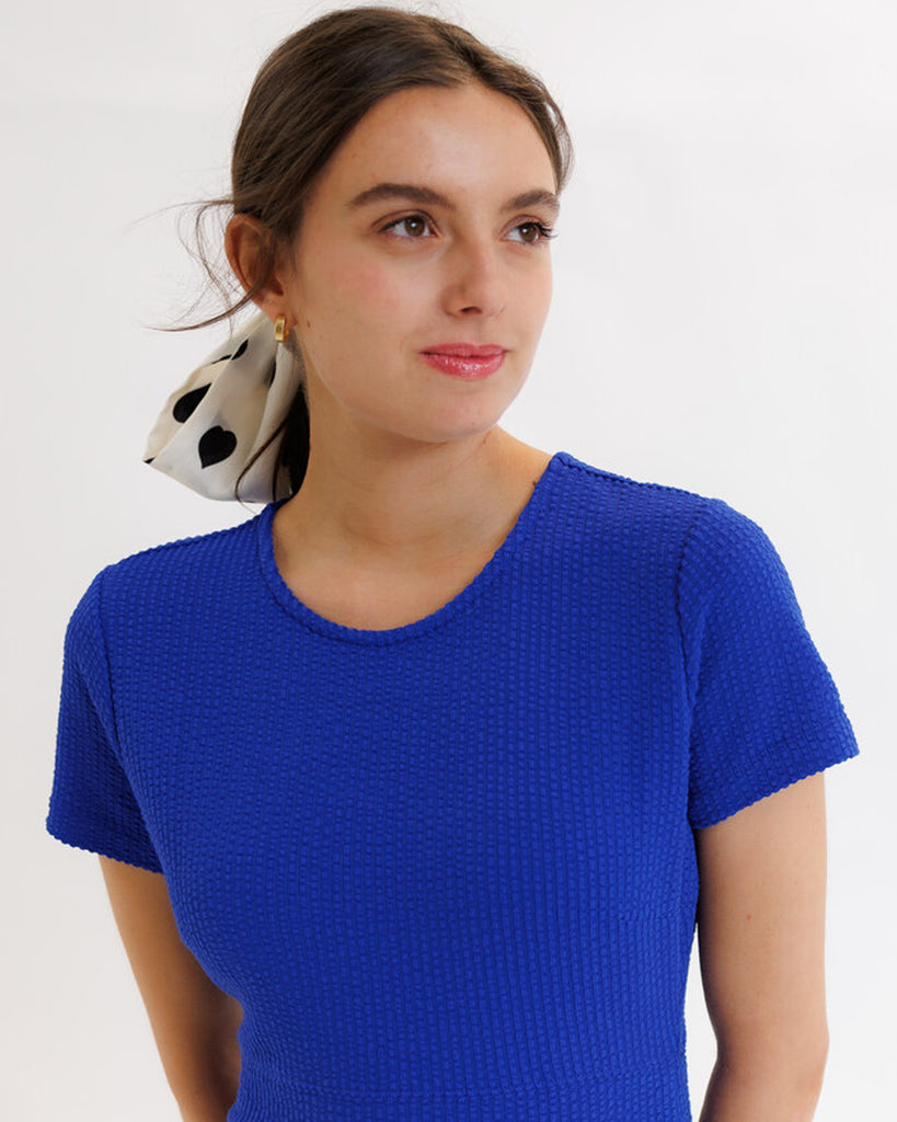 Model wearing a blue short sleeve, round neck, midi dress with pockets.