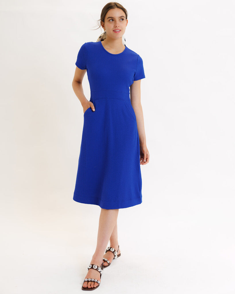 Model wearing a blue short sleeve, round neck, midi dress with pockets.
