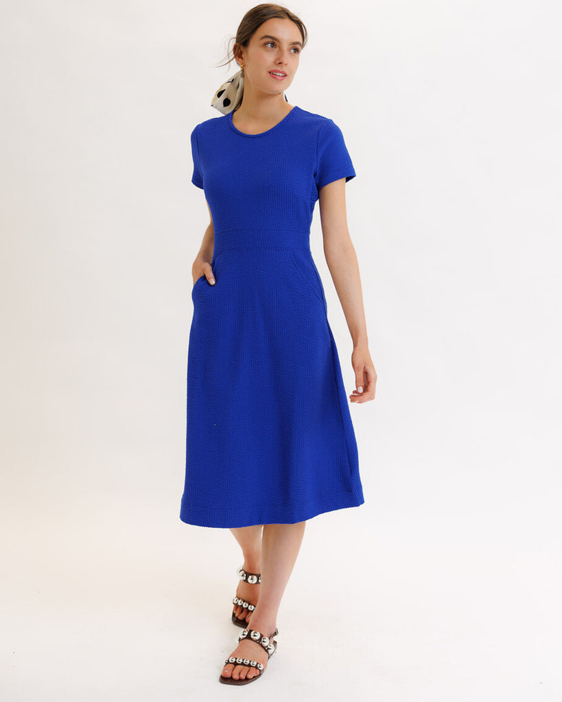 Model wearing a blue short sleeve, round neck, midi dress with pockets.