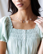 Woman wearing a light green top and a delicate necklace with small flowers.