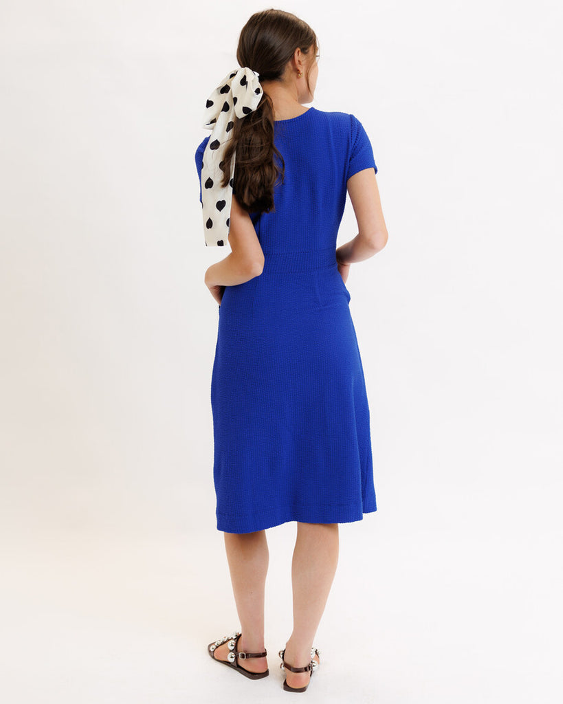 Model wearing a blue short sleeve, round neck, midi dress with pockets.