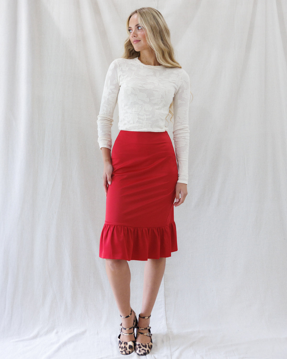 Front view of the cream floral open-knit long-sleeve tee tucked neatly into a high-waisted red ruffle-hem pencil skirt.