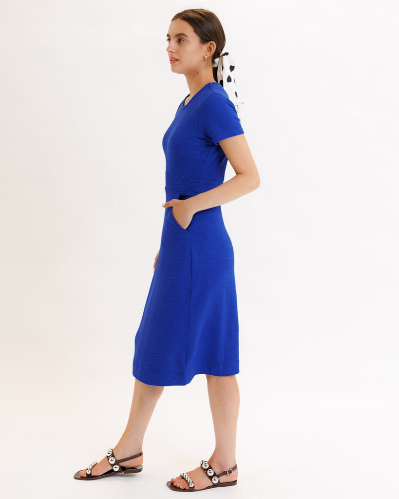 Model wearing a blue short sleeve, round neck, midi dress with pockets.