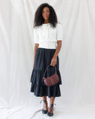 Model wearing a black tiered midi skirt styled smoothly at the waistband under a cream bow-tie short-sleeve cardigan.