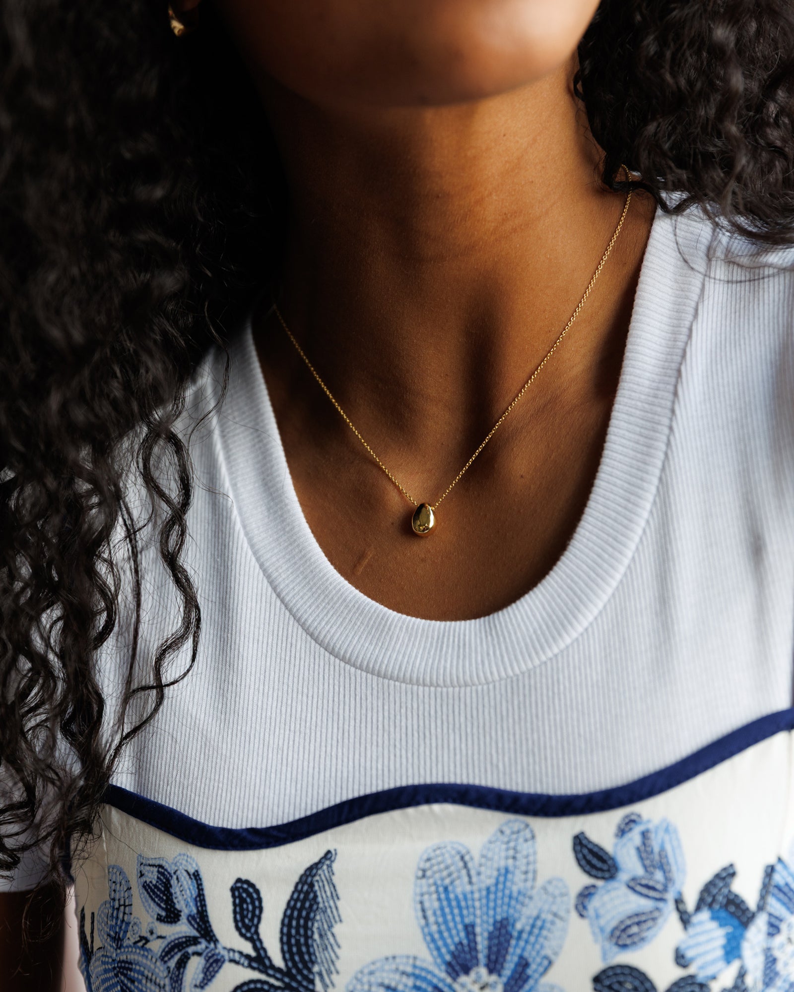 Close-up of a person wearing a delicate gold necklace with a small pendant.