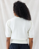 Back view highlighting the delicate pointelle stitch detail along the crew neckline, subtle shoulder gathers on the elbow-length sleeves, and fitted ribbed hem of the cream knit sweater top.
