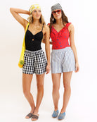 Two women wearing checkered shorts and colorful tops on a white background