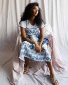 Woman wearing a white dress with blue floral patterns sitting on a white draped background