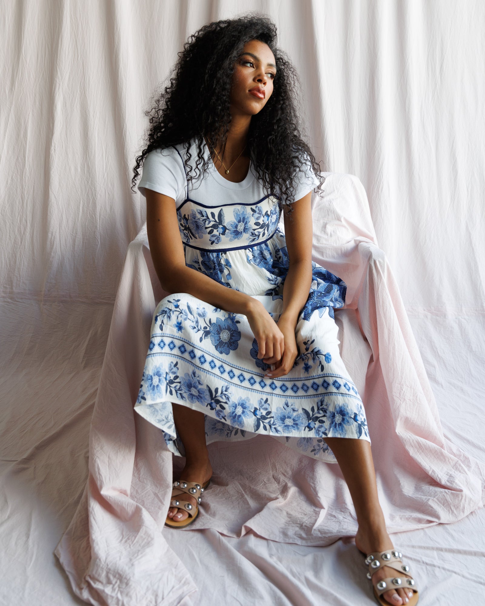 Woman wearing a white dress with blue floral patterns sitting on a white draped background