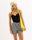 Woman wearing a black top, checkered shorts, and banana-themed headband with a yellow bag.