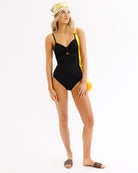 Woman wearing a black swimsuit with yellow accents on a white background