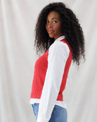 Side profile showing the slightly cropped length, deep sleeveless armholes, and wide ribbed hemband of the red cable-knit vest layered over a white shirt.