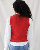 Back view highlighting the straight, tailored fit of the red knit vest with vertical cable and rib patterns, wide armhole ribbing, and waist-grazing ribbed hem.