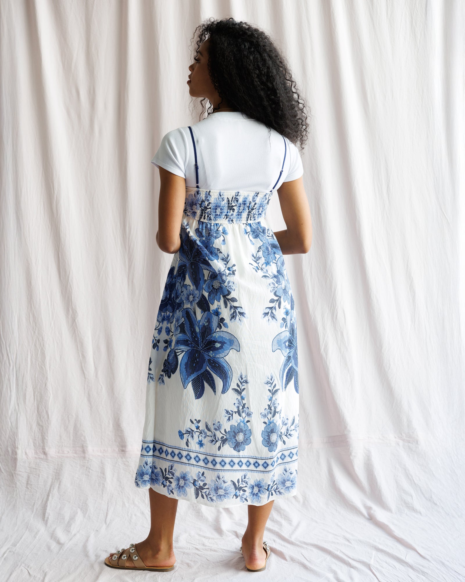 Person wearing a white t-shirt with a blue floral dress over it against a white curtain background