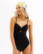 Woman wearing a black one-piece swimsuit and a banana-patterned headband on a white background