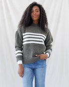 Front view highlighting the cozy mock neckline, horizontal white chest striping, and thick ribbed hem of the olive green crew-cut sweater.