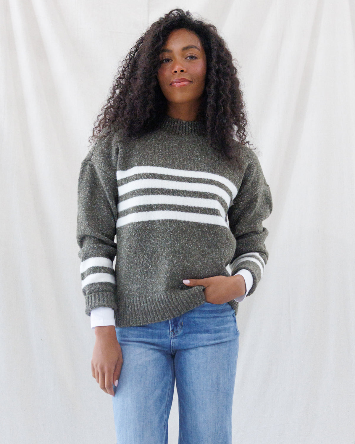 Front view highlighting the cozy mock neckline, horizontal white chest striping, and thick ribbed hem of the olive green crew-cut sweater.