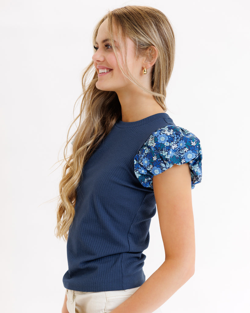 Model wearing a blue short sleeve knit tee with blue floral print puffed sleeves