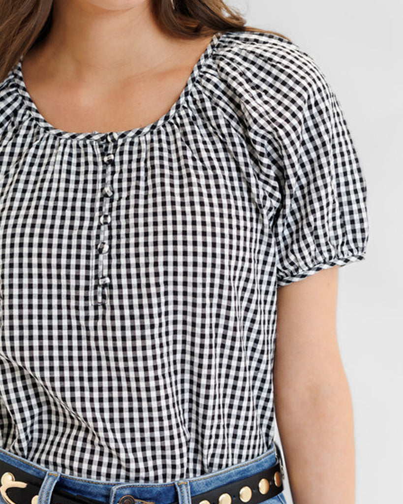 Model wearing a black and white gingham short sleeve scoop neck blouse.