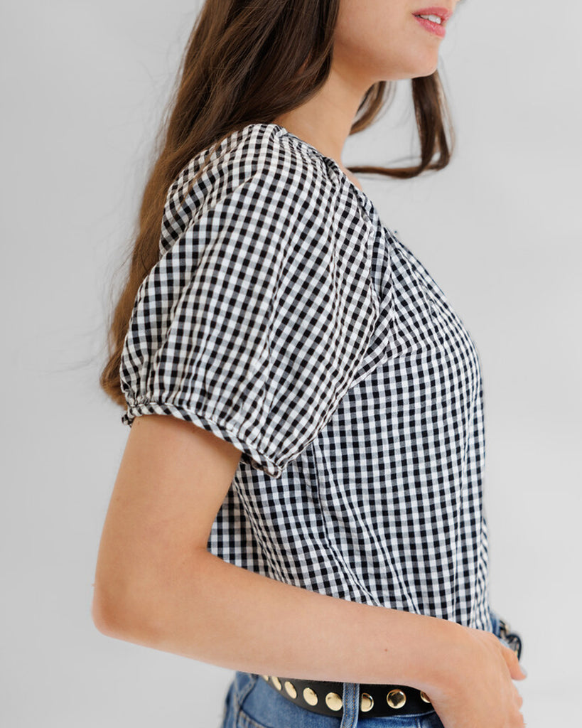 Model wearing a black and white gingham short sleeve scoop neck blouse.