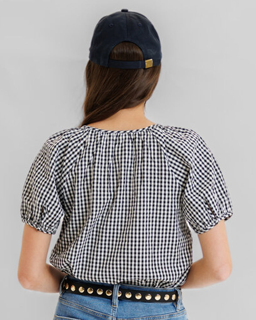 Model wearing a black and white gingham short sleeve scoop neck blouse.