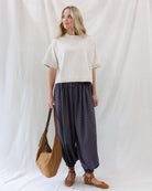 Front full-length view of the boxy beige short-sleeve knit sweater paired untucked with high-waisted navy and red plaid balloon pants.