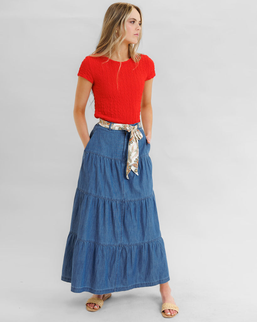 Model wearing a blue denim tiered maxi skirt with pockets.