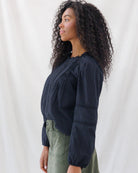 Side profile showing the relaxed drape and slight shoulder puff of the black long-sleeve blouse, detailed with subtle horizontal lace trim along the sleeves.