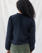 Back view highlighting the clean, easy-fitting silhouette of the black peasant top with a delicate ruffle-trimmed collar, keyhole loop closure, and hip-length hem.