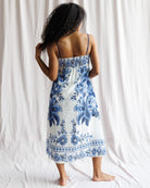 Woman wearing a blue floral dress standing against a white curtain