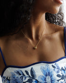 Close-up of a person wearing a gold necklace with a small pendant, against a blurred background.