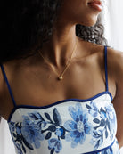 Woman wearing a white dress with blue floral embroidery and a gold necklace.