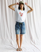 Person wearing a white t-shirt with a graphic design and denim shorts against a plain background