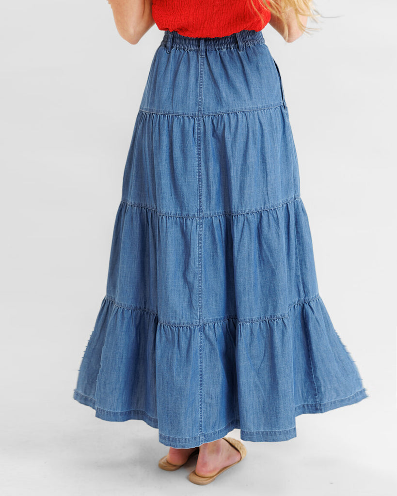 Model wearing a blue denim tiered maxi skirt with pockets.
