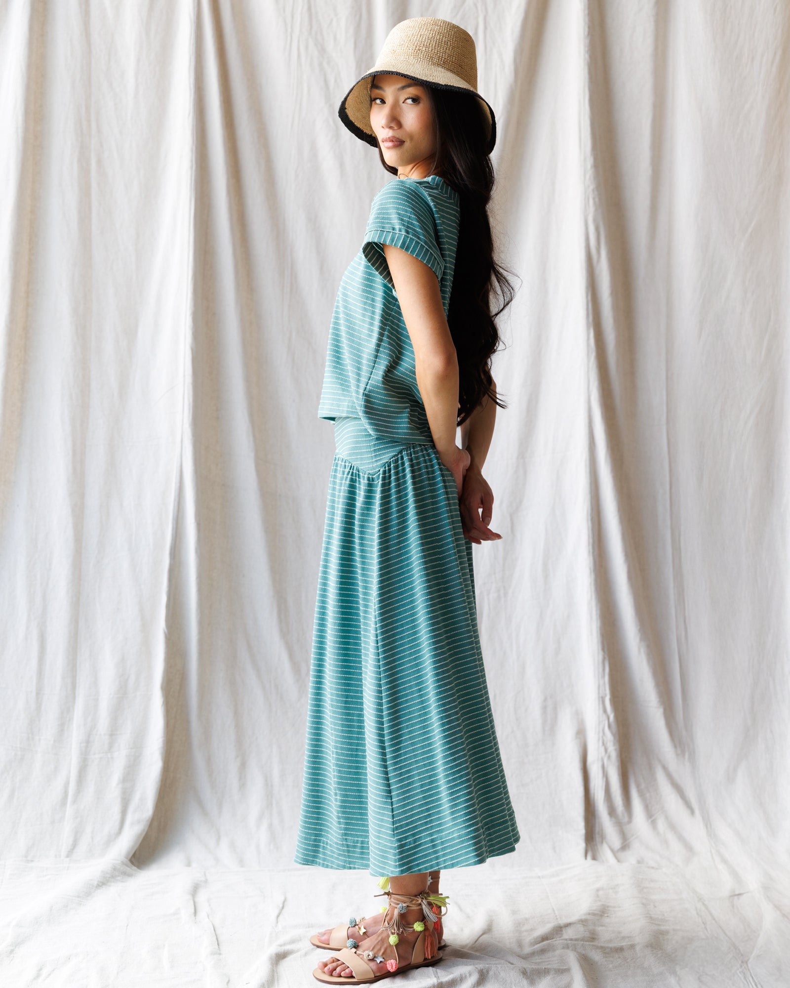Woman wearing a teal dress and hat against a white curtain background