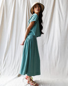 Woman wearing a teal striped dress and hat against a white curtain background